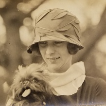 Portrait photo of young woman in 1920s hat holding fluffy dog