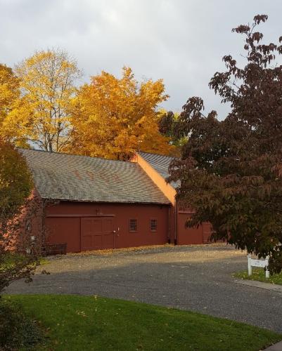 color photo of a red barn with golden autumn leaves on trees behind