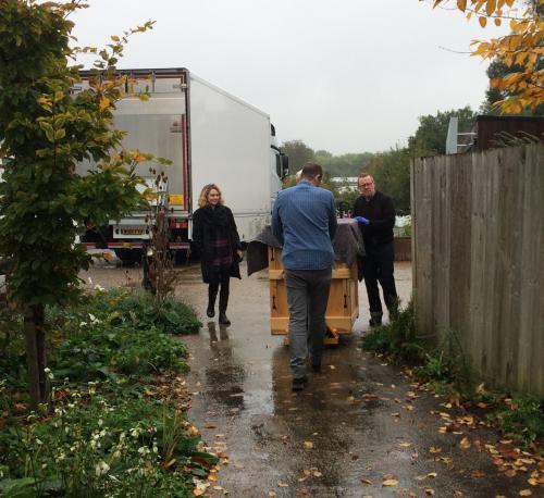 color photo of two men moving a crate, a woman walking beside it, a truck in back