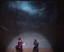 two men in costume in front of a projected scene of a castle in fog