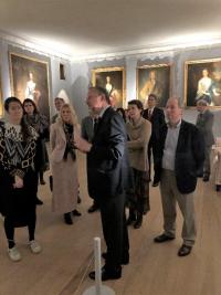 color photo of people listening to man speak in a room with paintings